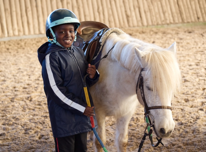 Un petit garçon de l'Académie Younus pose à côté de son poney après une initiation d'équitation.